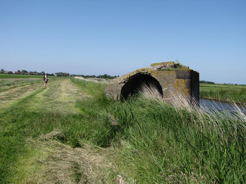 sexbierumer vaart_met_bruggehoofd_NFLS.jpg - Het laatste stuk van het  Barradeelster paed is gelukkig door een boer gemaaid, dat loopt stukken lichter! Het bouwwerk rechts is een landhoofd van een verdwenen spoorbrug van de NFLS (Noord-Friesche Locaalspoorweg). De spoorlijn is in de jaren dertig van de vorige eeuw reeds stilgelegd. Dat het reeds een tijdje geleden is merk je ook aan het feit dat er niets in het landschap terug te vinden is van de spoordijk die naar de spoorbrug toe moet hebben geleid.